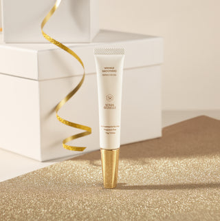 Skincare eye cream with gold cap and packaging on a glittery surface