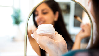 Woman looking down at Intense Barrier Cream moisturizer in front of a mirror.