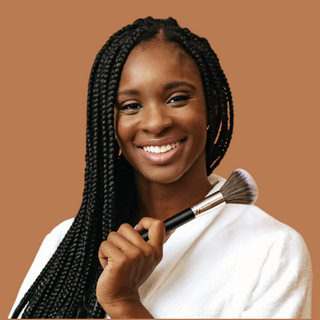 black makeup artist with braids, holding makeup brush on tan background.