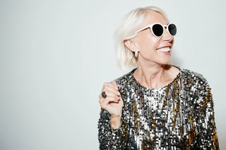 woman in sunglasses smiling with sequin top on white background