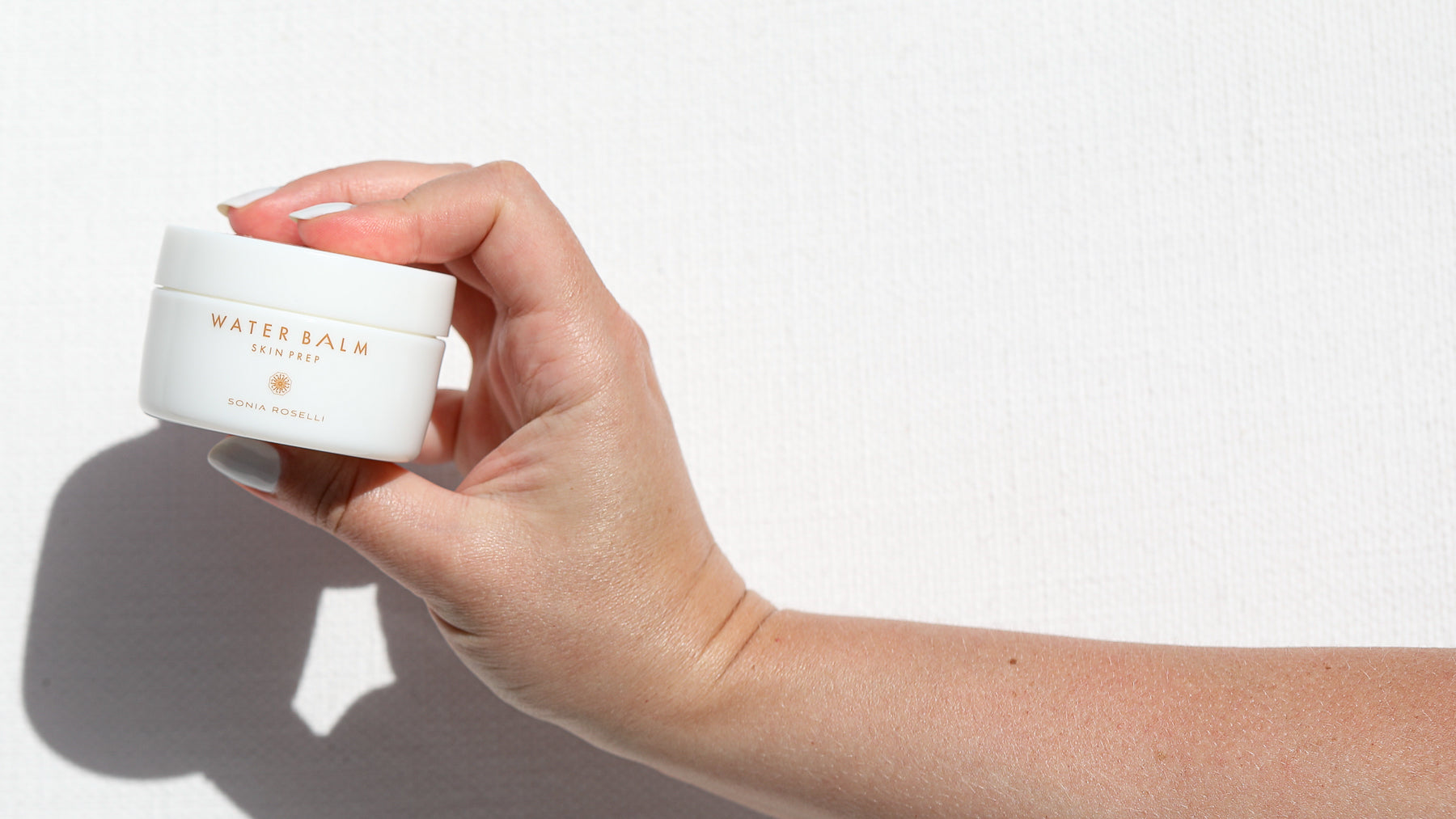Water Balm held up in a hand on white backdrop
