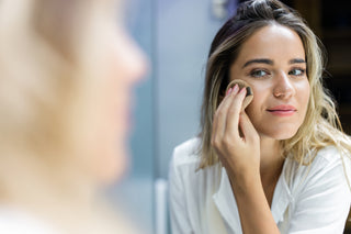 blonde woman applying foundation in mirror