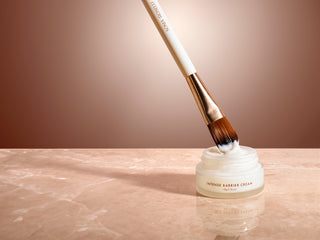 a skin prep brush dipped in intense barrier cream on marble top and tan background