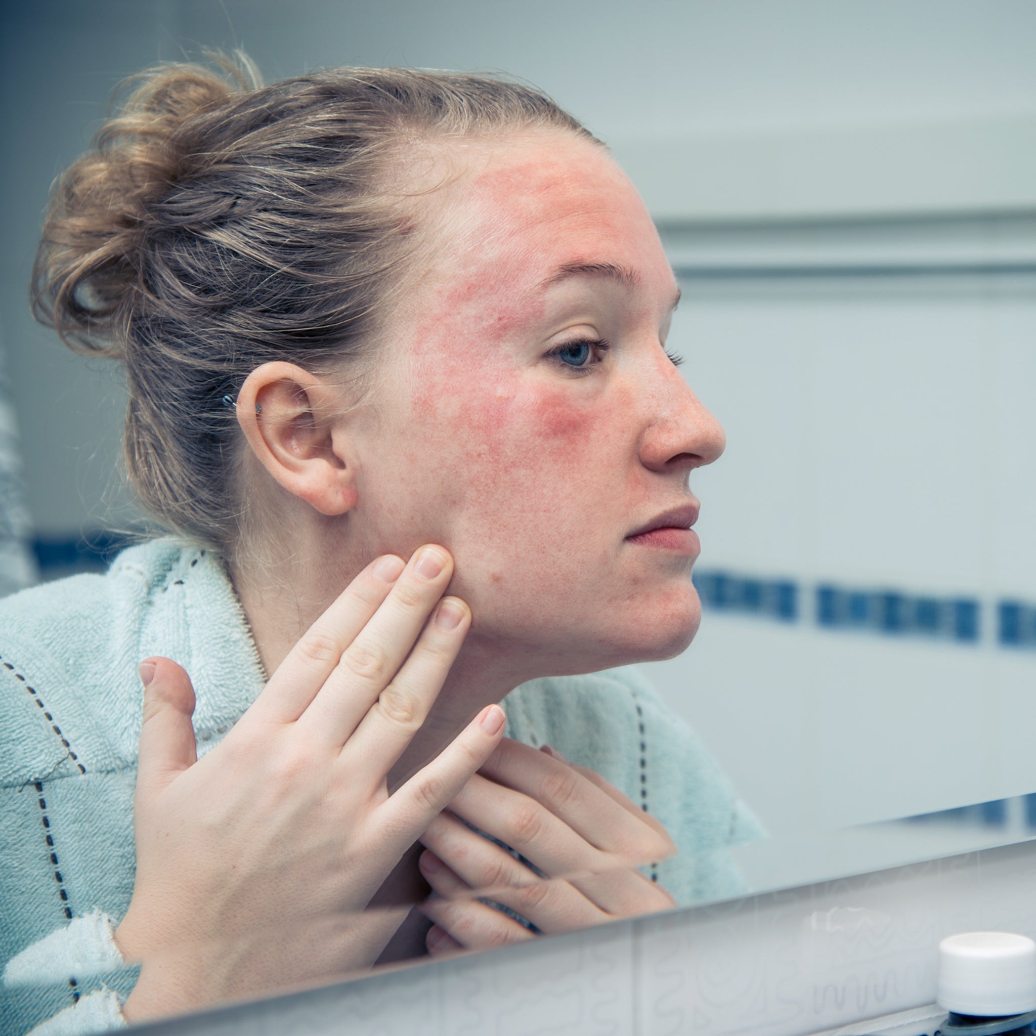 Woman looking in the mirror at her skin wondering why it is dull and sensitive.