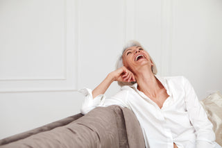 mature woman laughing, wearing white shirt sitting on sofa