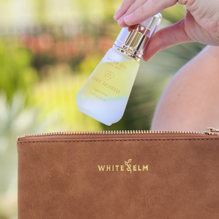 Hand holding Sonia Roselli Water Oil bottle above a White Elm cosmetic bag
