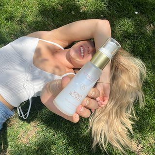 Woman laying down in grass holding Water Elixir up to the sun