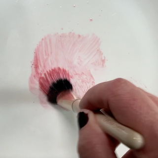 Makeup brush in hand, blending blush with Water Elixir to make a liquid blush