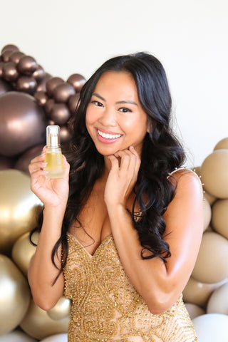 woman holding skincare bottle with gold dress and balloons in background