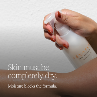 A hand with orange-red nail polish pumps a white spray bottle onto an arm, with text reading 'Skin must be completely dry. Moisture blocks the formula.