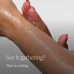 A close-up of a person's forearm and hand with a glossy white cream or powder being rubbed in, overlaid with the text 'See it gathering? That's it working.' on a soft light gray background.