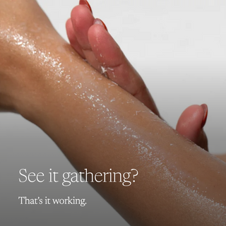 A close-up of a person's forearm and hand with a glossy white cream or powder being rubbed in, overlaid with the text 'See it gathering? That's it working.' on a soft light gray background.