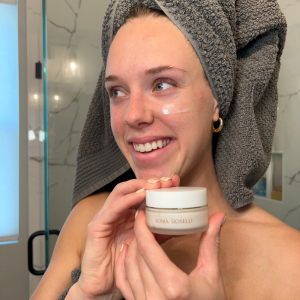 Woman with towel over hair, holding Intense barrier cream moisturizer jar up in front of her