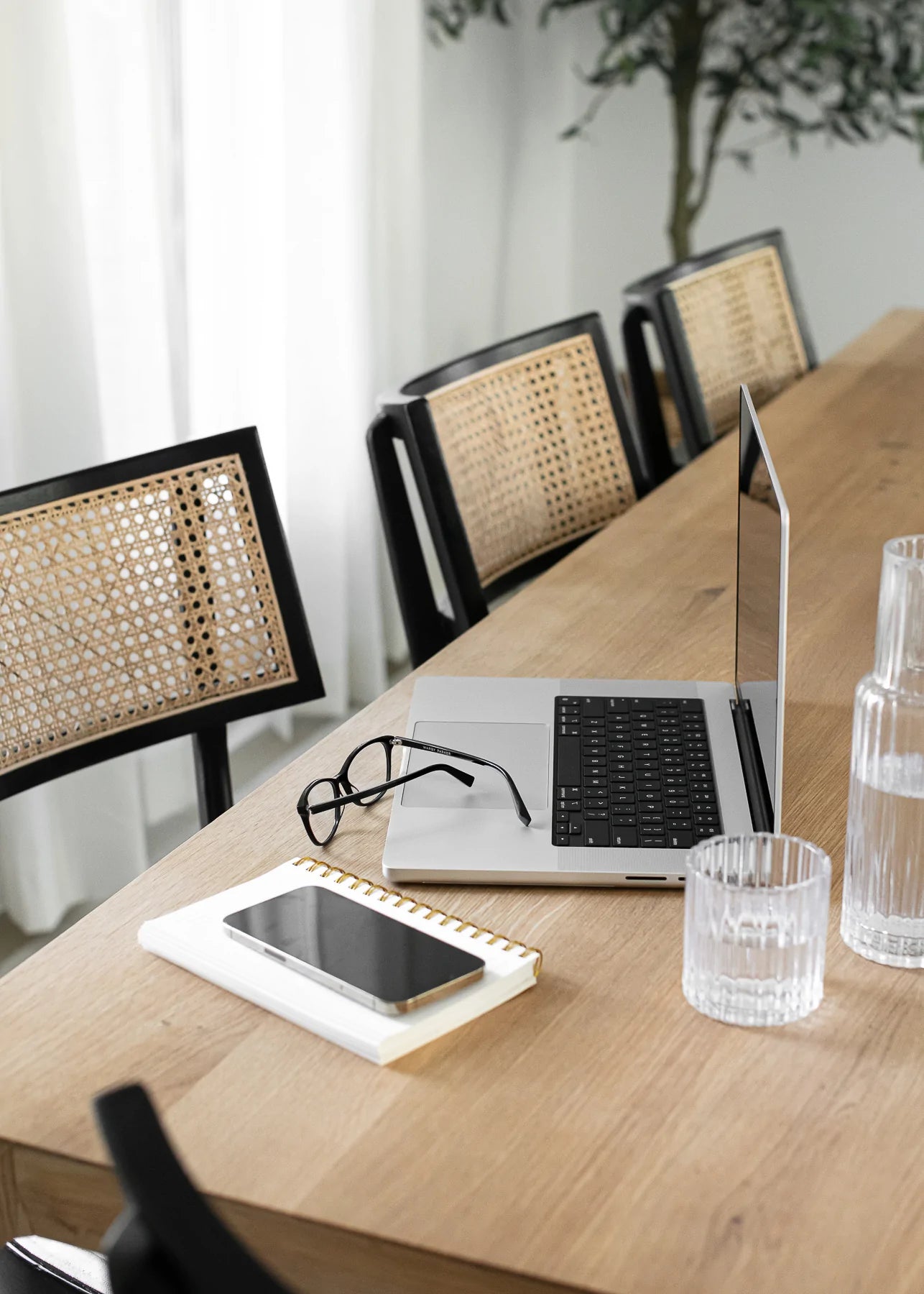 A laptop, glasses, phone, notebook, and glass of water sit on a table.