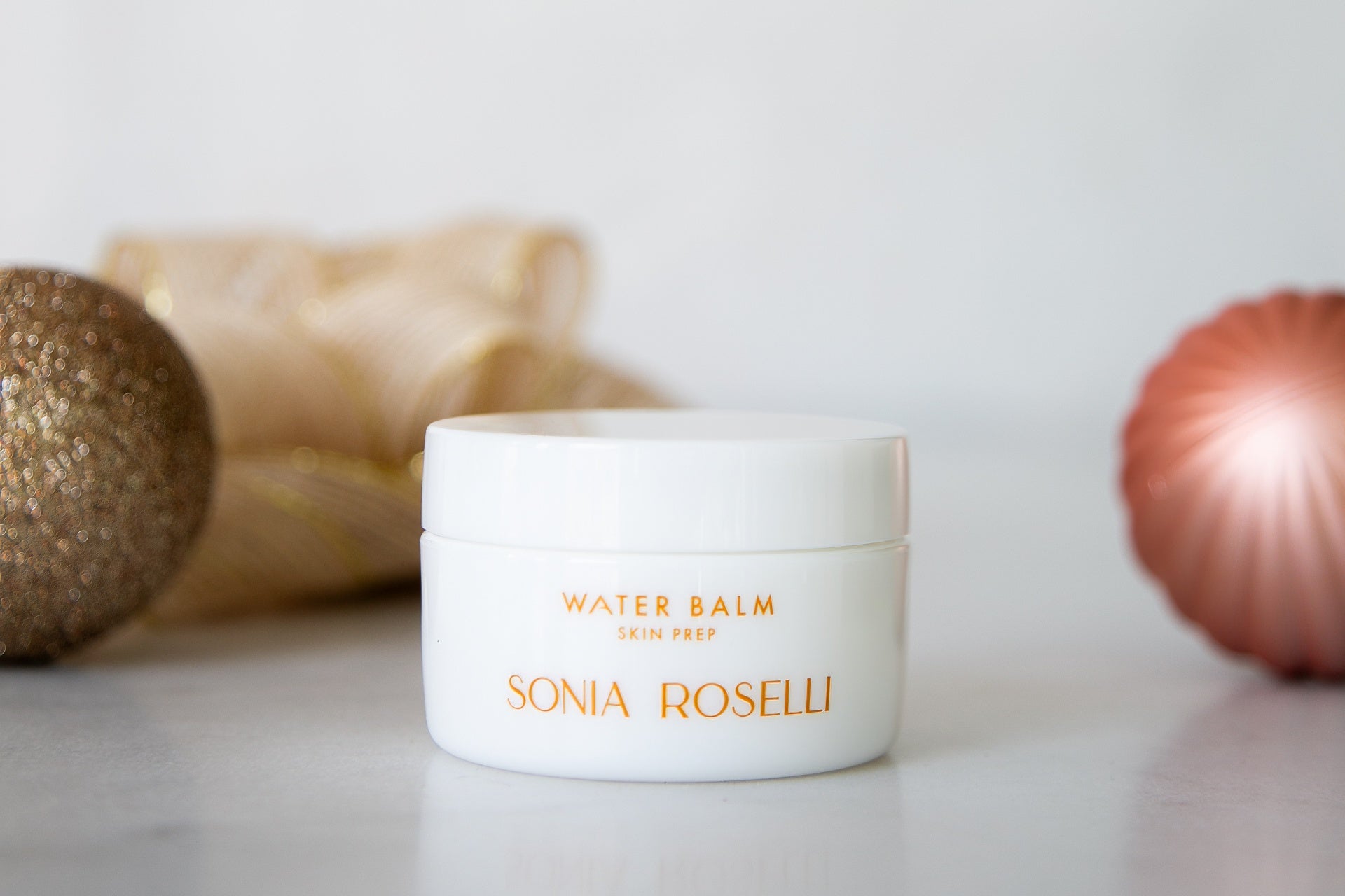 A jar of Water Balm in front of ornaments and tulle. 