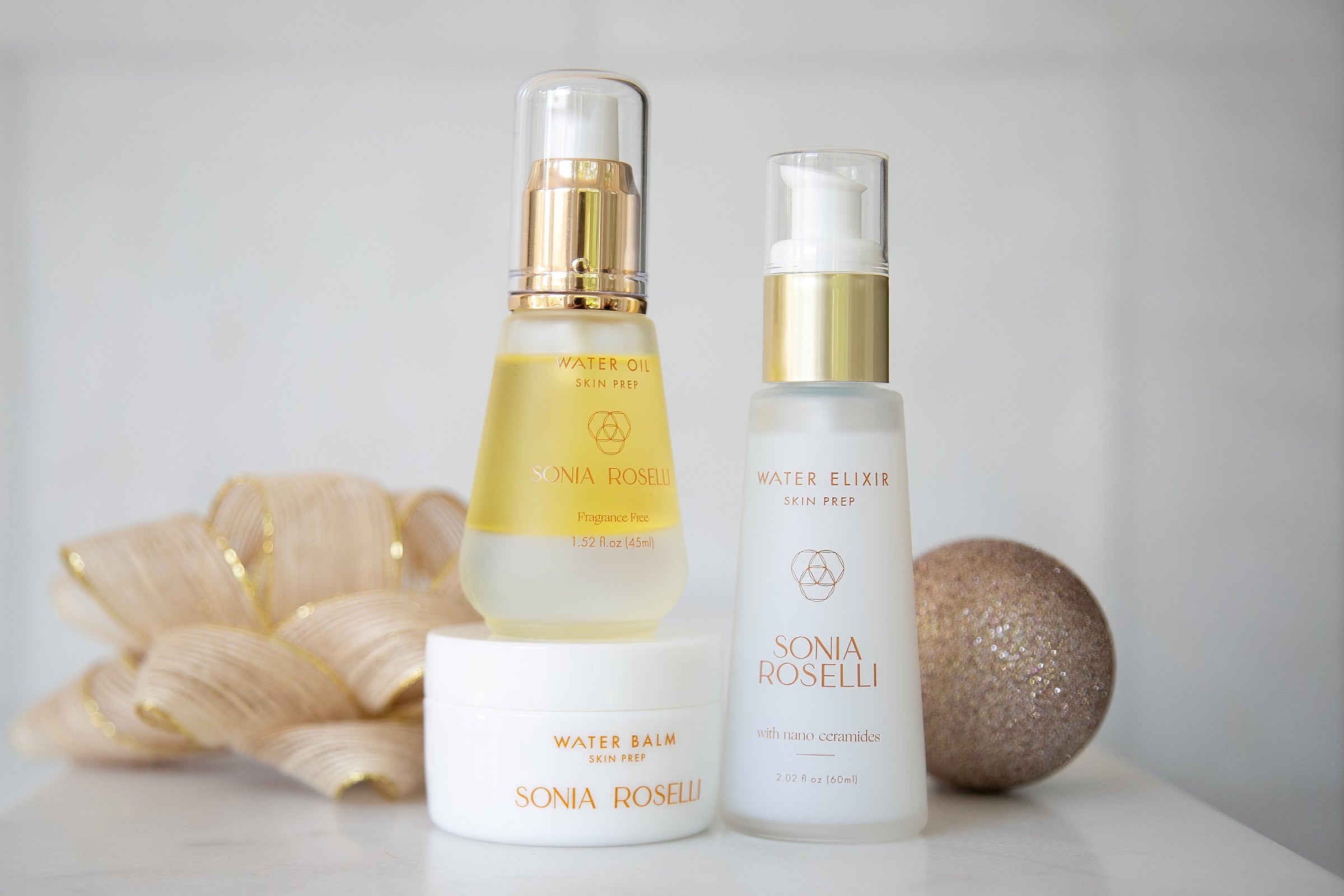 Water Elixir, Water Balm, and Water Oil in front of an ornament and bow.