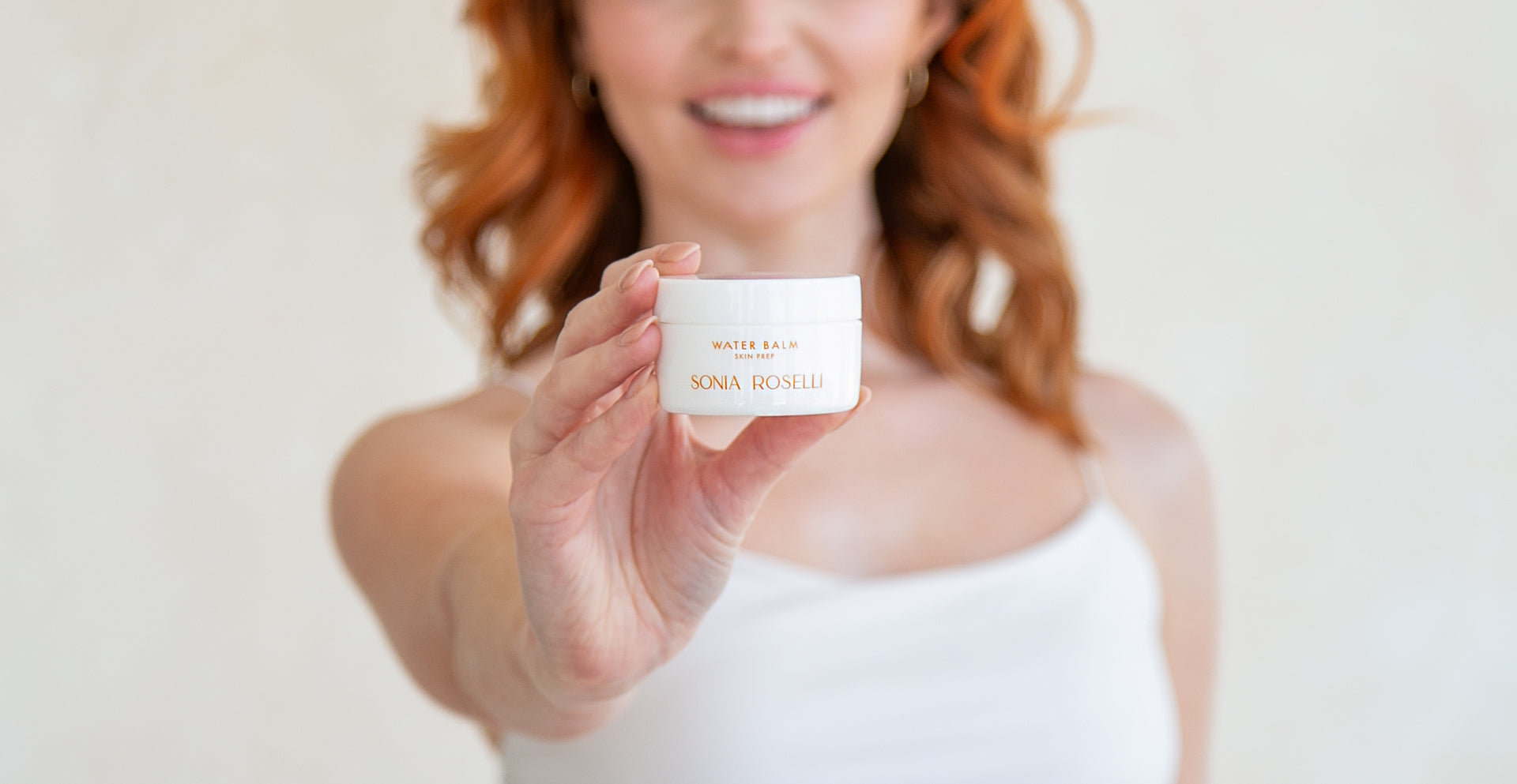 In a delightful moment captured, a joyful woman holds a jar of Sonia Roselli Beauty's Water Balm moisturizer, her radiant smile reflecting the satisfaction and confidence that comes from using this hydrating skincare product, which promises soft and glowing skin.