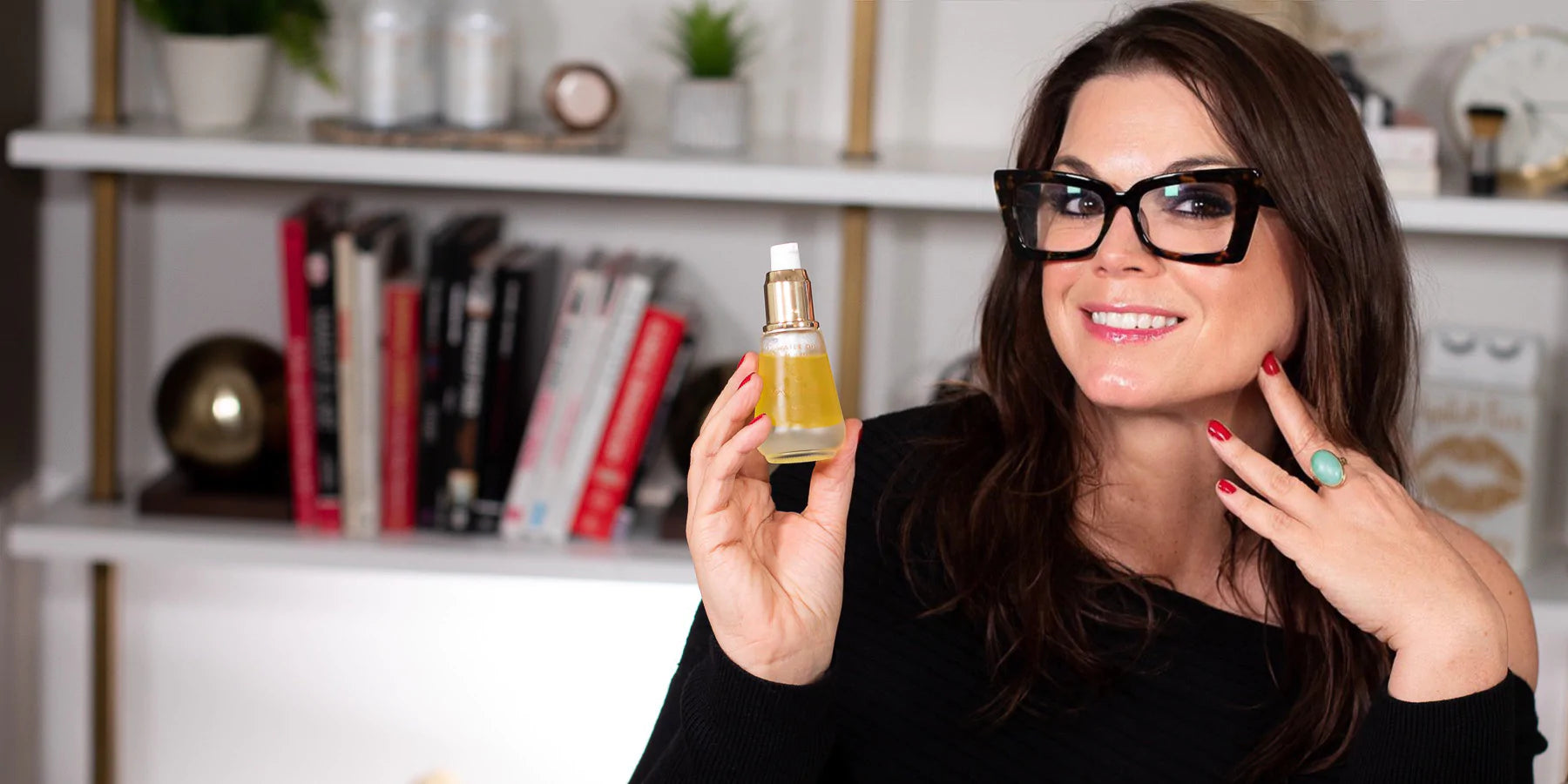 Sonia Roselli smiling to the camera showing off fabulous makeup and glowing skin while holding Water Oil facial serum and oil.
