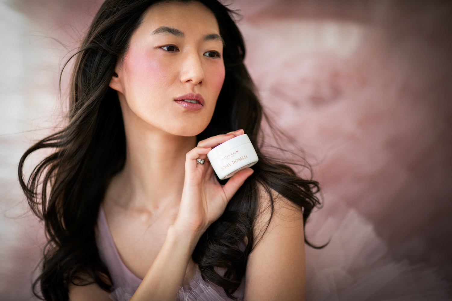 asian woman in pink dress holding water balm near face