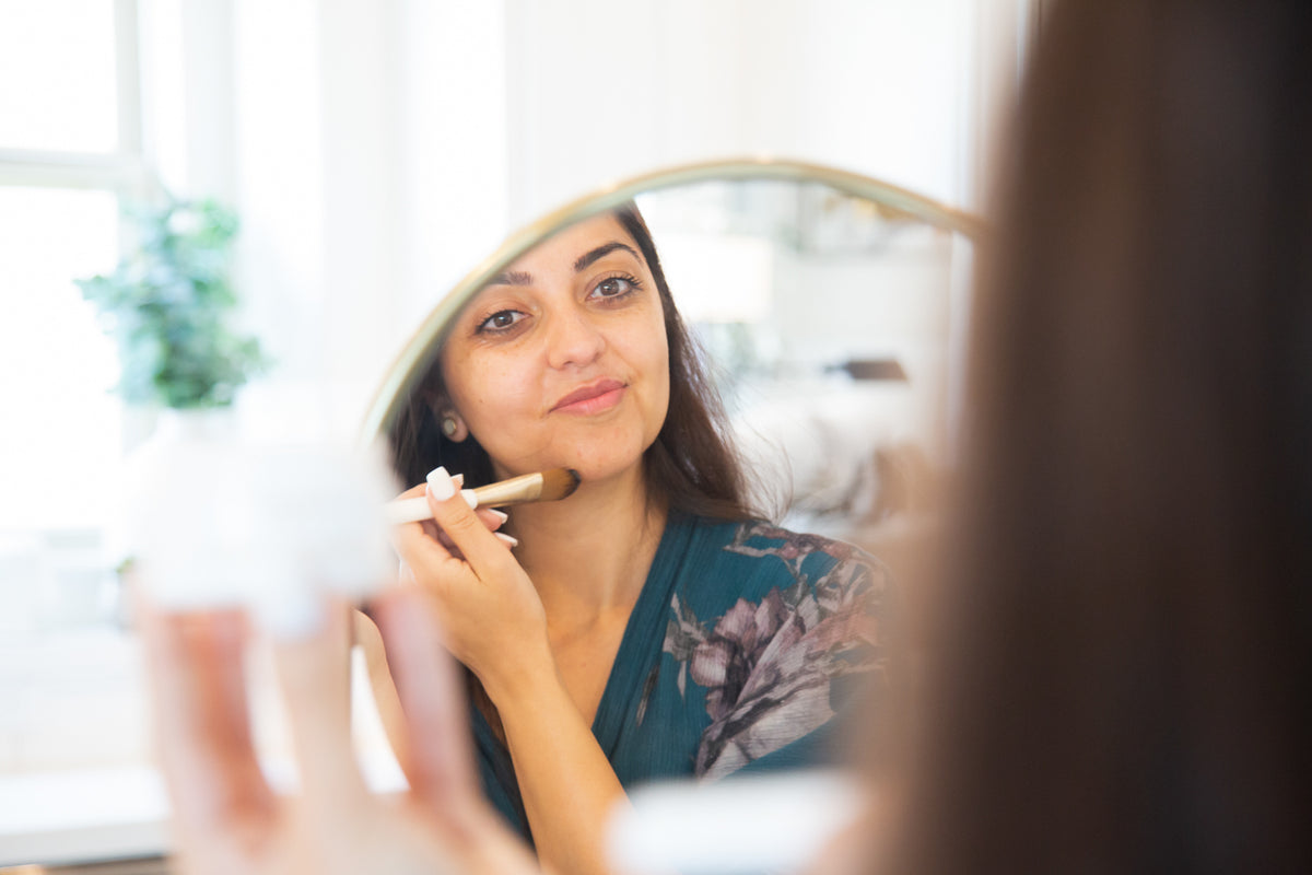 Woman looking in the mirror applying Intense Barrier Cream being applied with a brush 