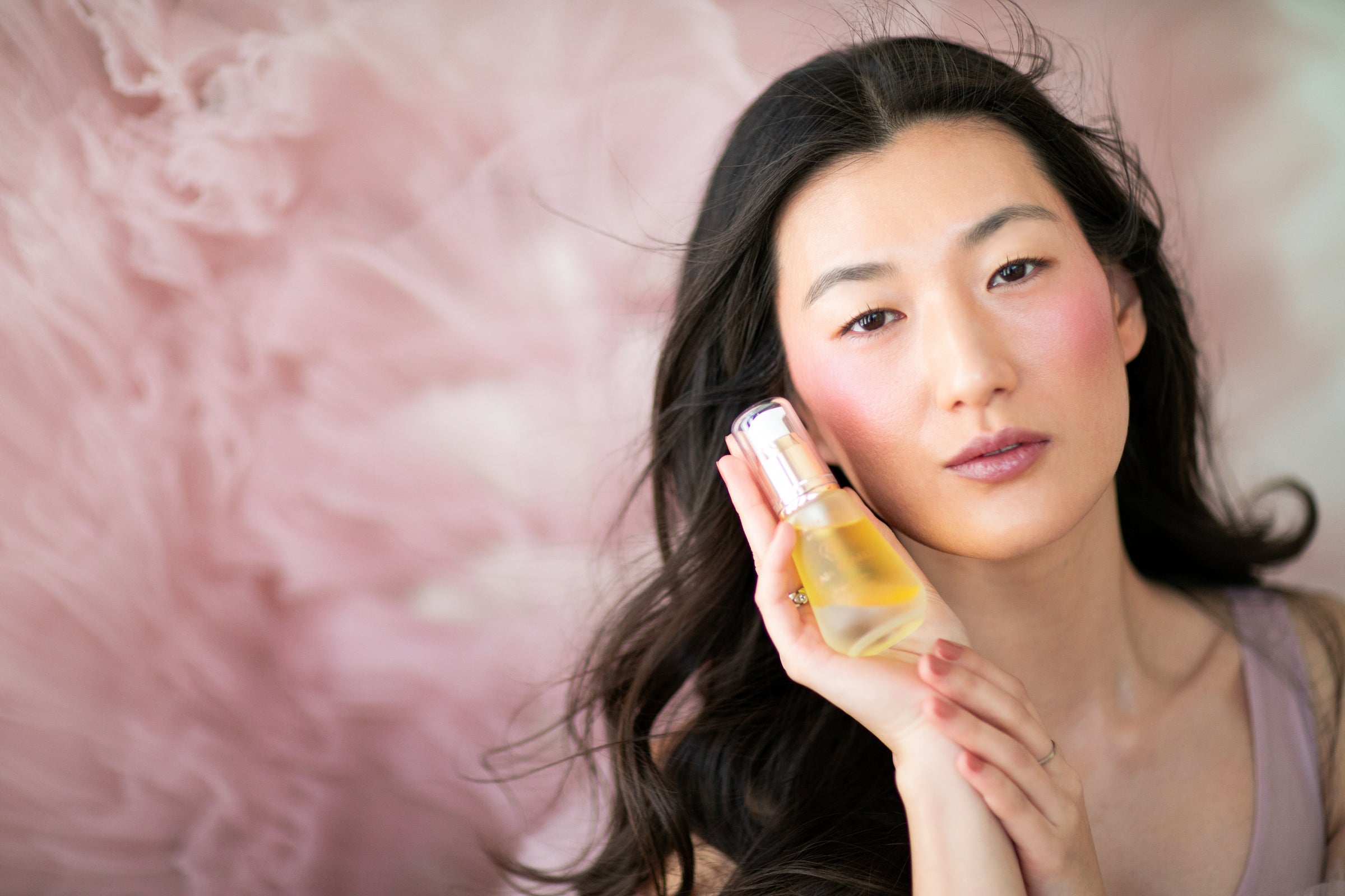 Woman holding Water Oil serum in front of pink tulle.