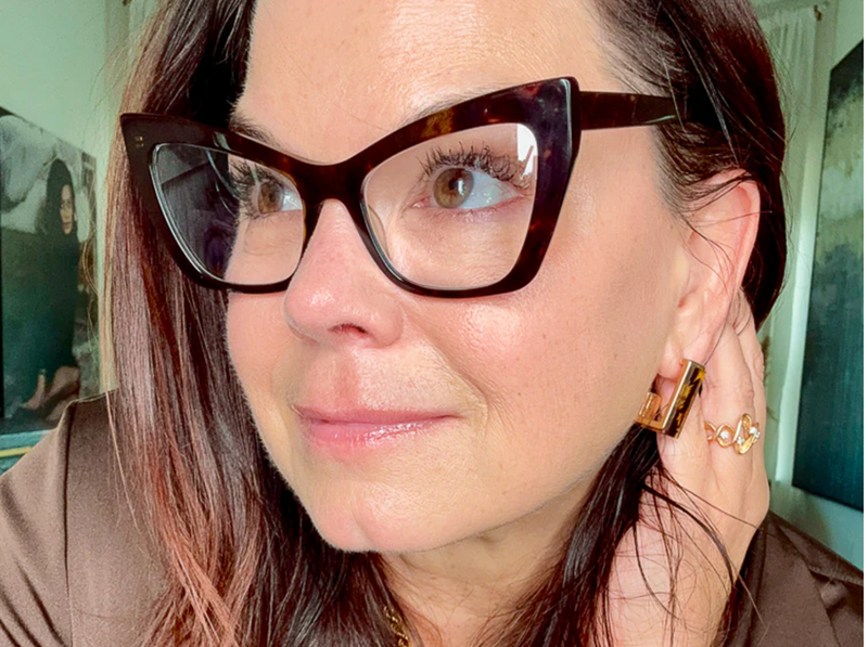 Close-up of a person wearing tortoiseshell glasses and matching earrings.