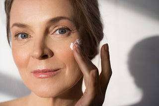 mature woman applying skincare cream on face white shadow background