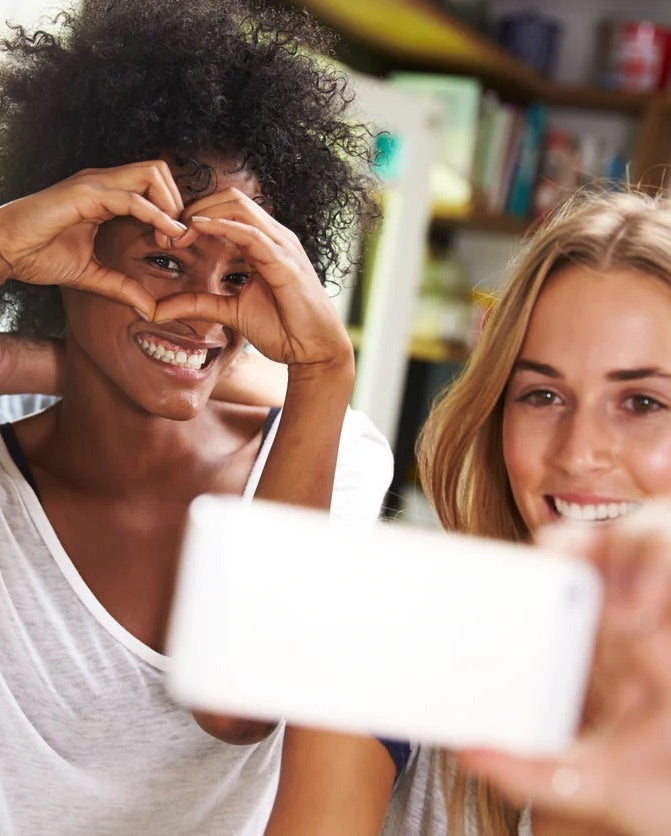 Two women stand side by side, smiling and forming heart shapes with their hands as a symbol of unity and love. They are participating in the Sonia Roselli Beauty Ambassador Program, showcasing their enthusiasm and passion for beauty.