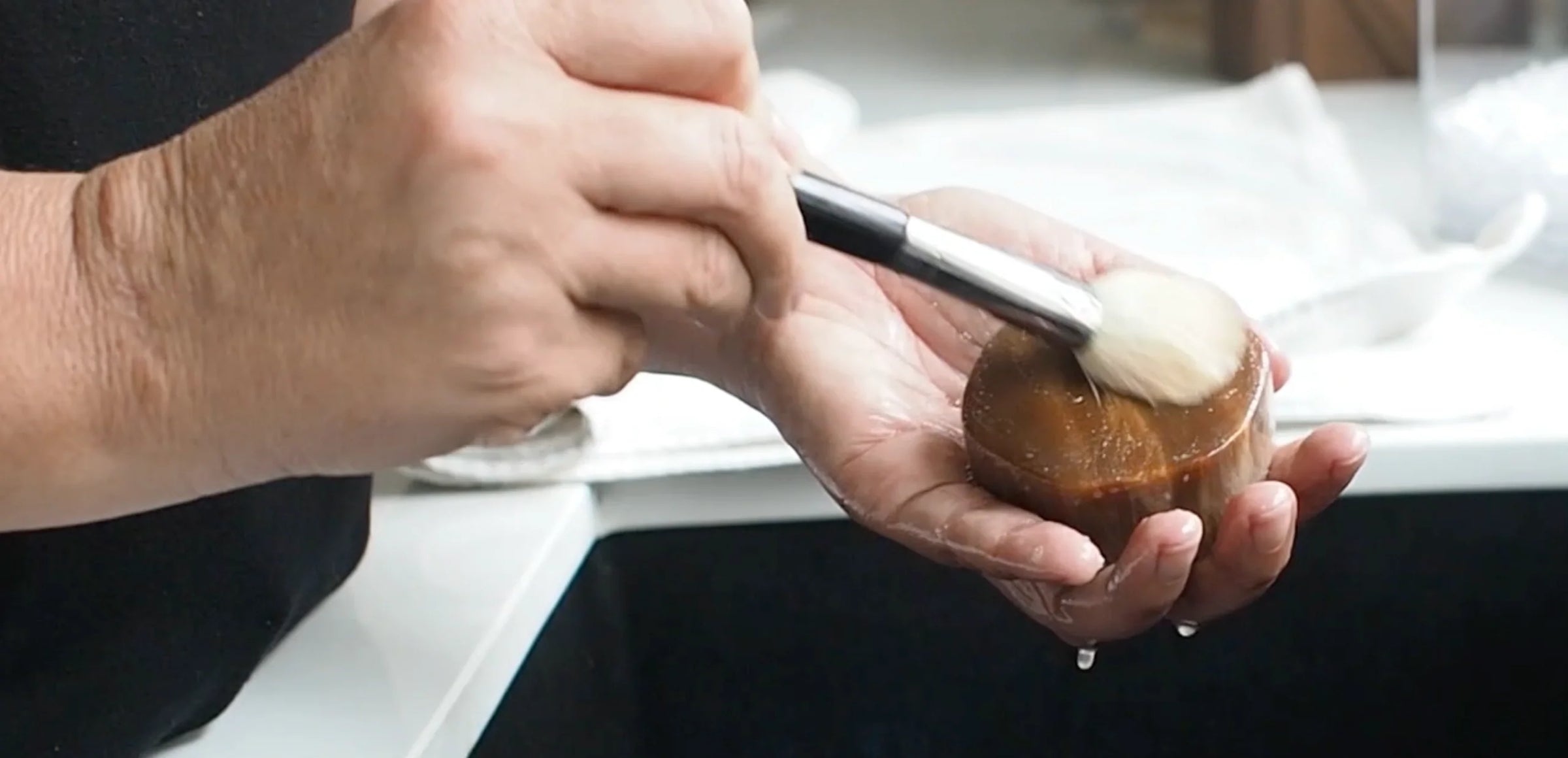 Hands using tiger's eye to clean a makeup brush over sink