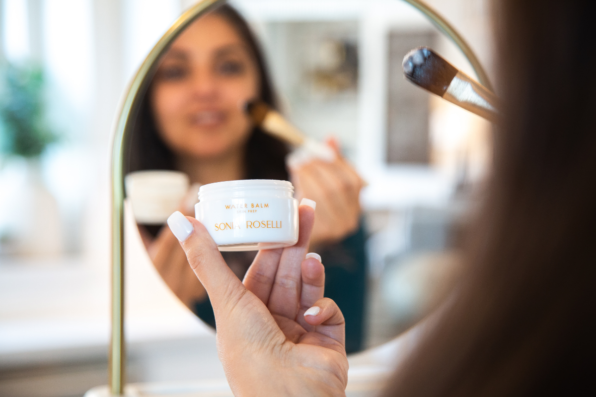 Woman applying Water Balm with Skin Prep brush, looking in the mirror