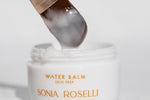 Close-up of Sonia Roselli Beauty Water Balm Skin Prep with a brush lifting the silky balm texture from the jar, showing its lightweight, hydrating consistency.