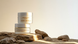 Sonia Roselli barrier repair moisturizers - Water Balm and Intense Barrier Cream in frosted glass jars with gold caps on desert sandstone