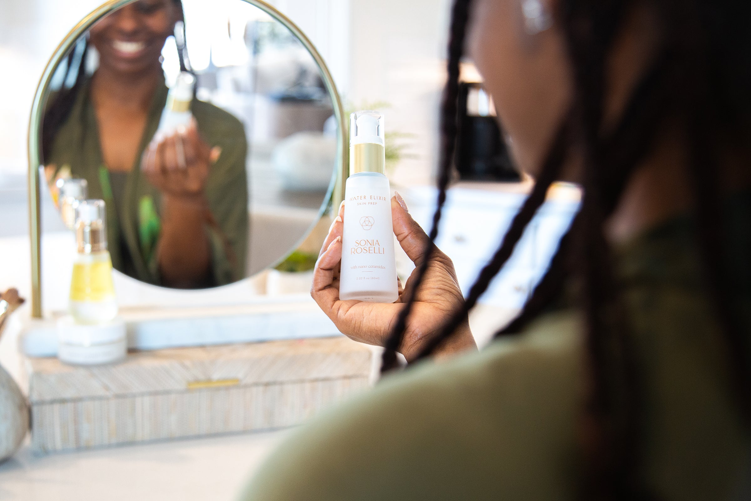 In front of a well-lit mirror, a woman confidently holds a bottle of Sonia Roselli Beauty's Water Elixir, her reflection showcasing a sense of empowerment and radiance. This image encapsulates the transformative potential of the product, promising a revitalized and luminous complexion.