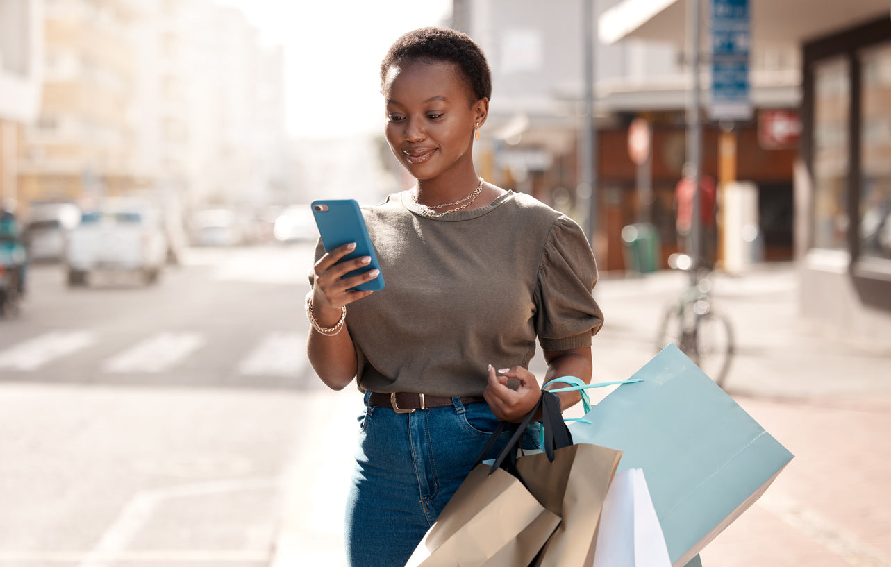 Woman holding shopping bags and looking at her phone smiling.