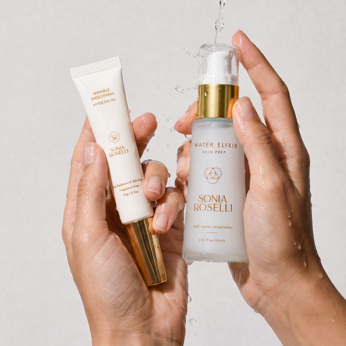 Two hands holding skincare products from Sonia Roselli against a light gray background with water droplets splashing around the pump bottle. One hand holds a white tube with a gold cap labeled 'Sonic Smoothing Serum', and the other holds a frosted bottle with a gold pump labeled 'Water Elixir Skin Prep'.