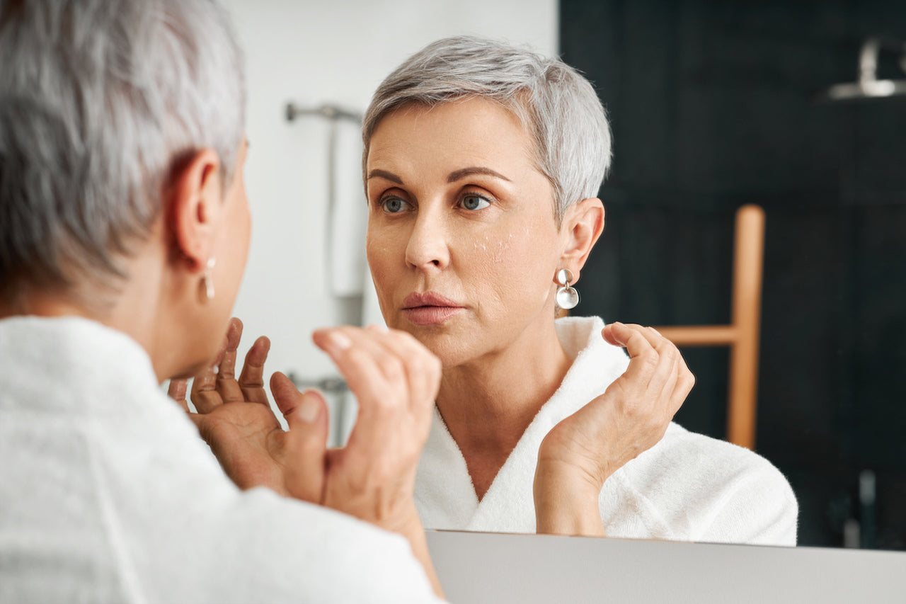 Woman looking at face in mirror while applying Intense barrier Cream with fingers