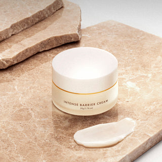 A jar of Intense Barrier Cream is displayed on a marble surface with a small amount of the cream placed beside it, showcasing its texture.