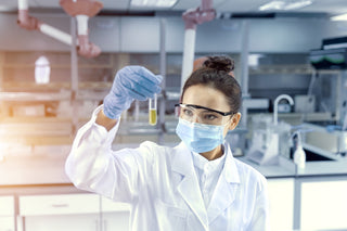 Female chemist wearing PPE, holding up test tube. 