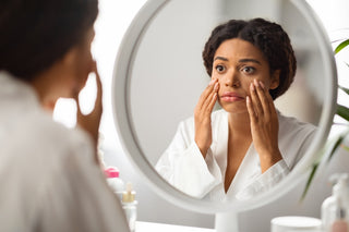 black woman in robe looking in mirror at her dry skin
