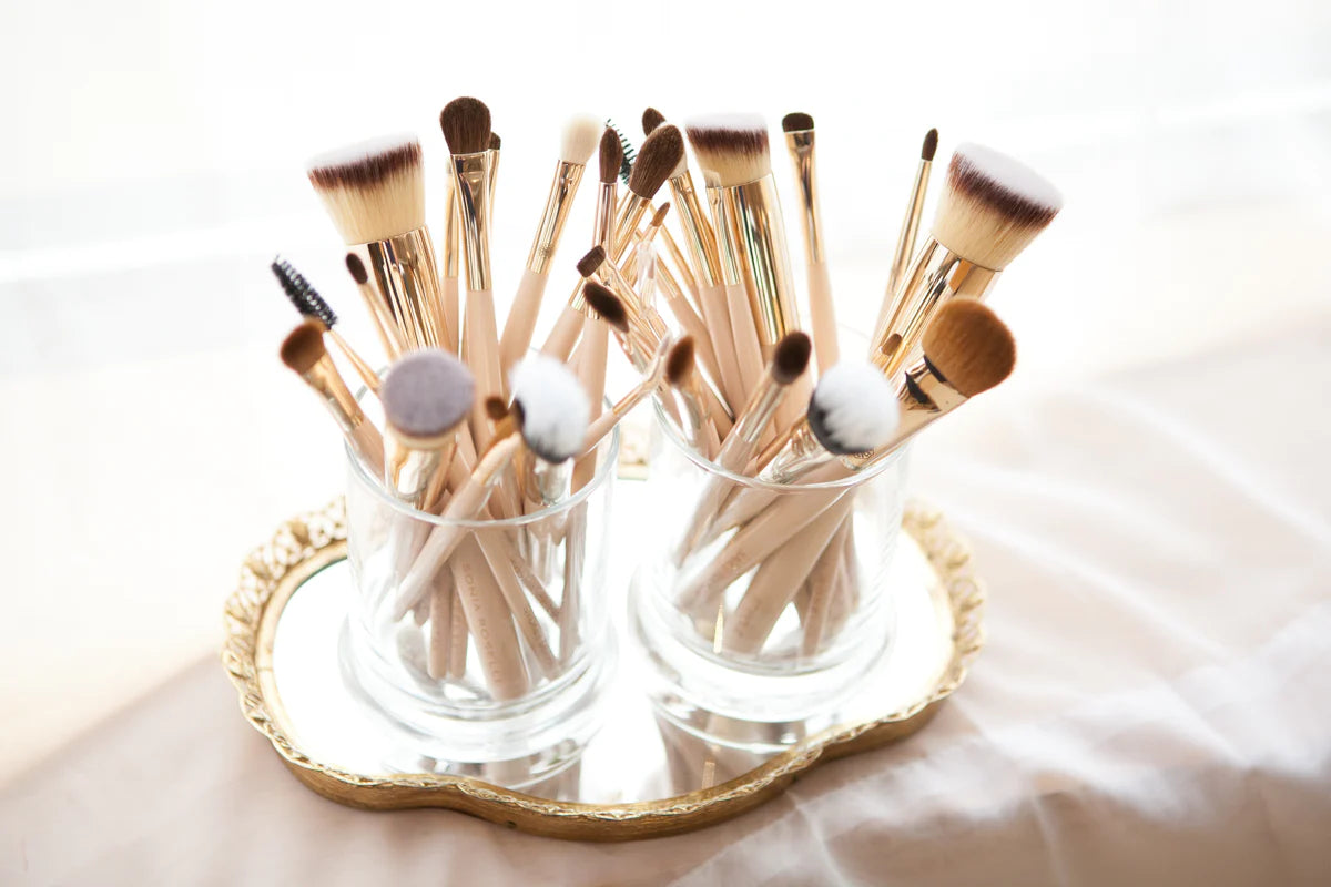 Makeup brushes in two glass jars on gold mirrored tray