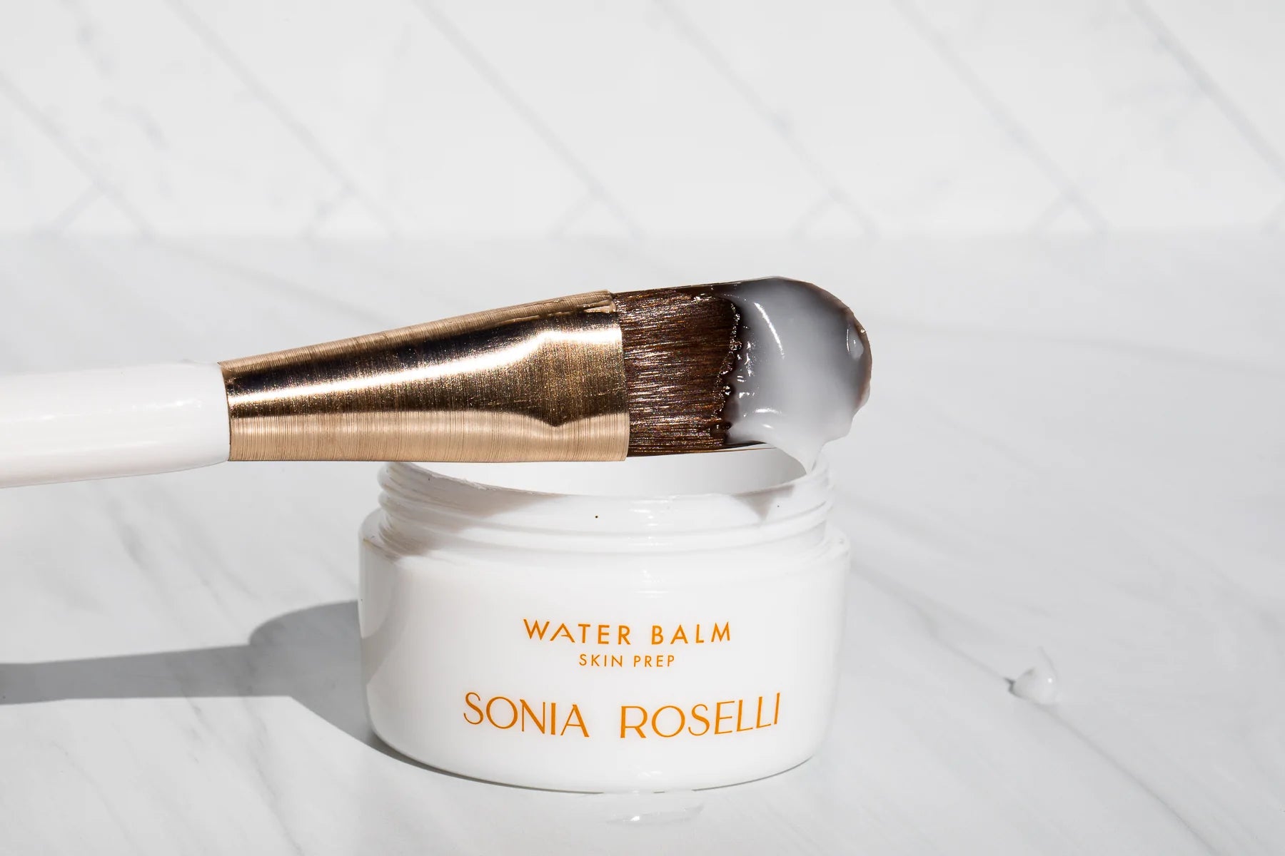 Skin Prep Brush that has been dipped in product, propped up on Water Balm jar. 