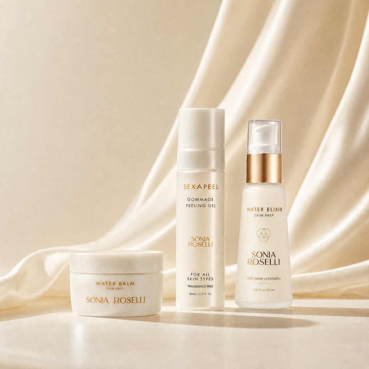 Three Sonia Roselli skincare products arranged on a draped cream satin fabric background: a Water Balm jar, a Cloud-Make Peeling Gel bottle, and a Water Elixir Glow Spray bottle with a metallic gold collar.
