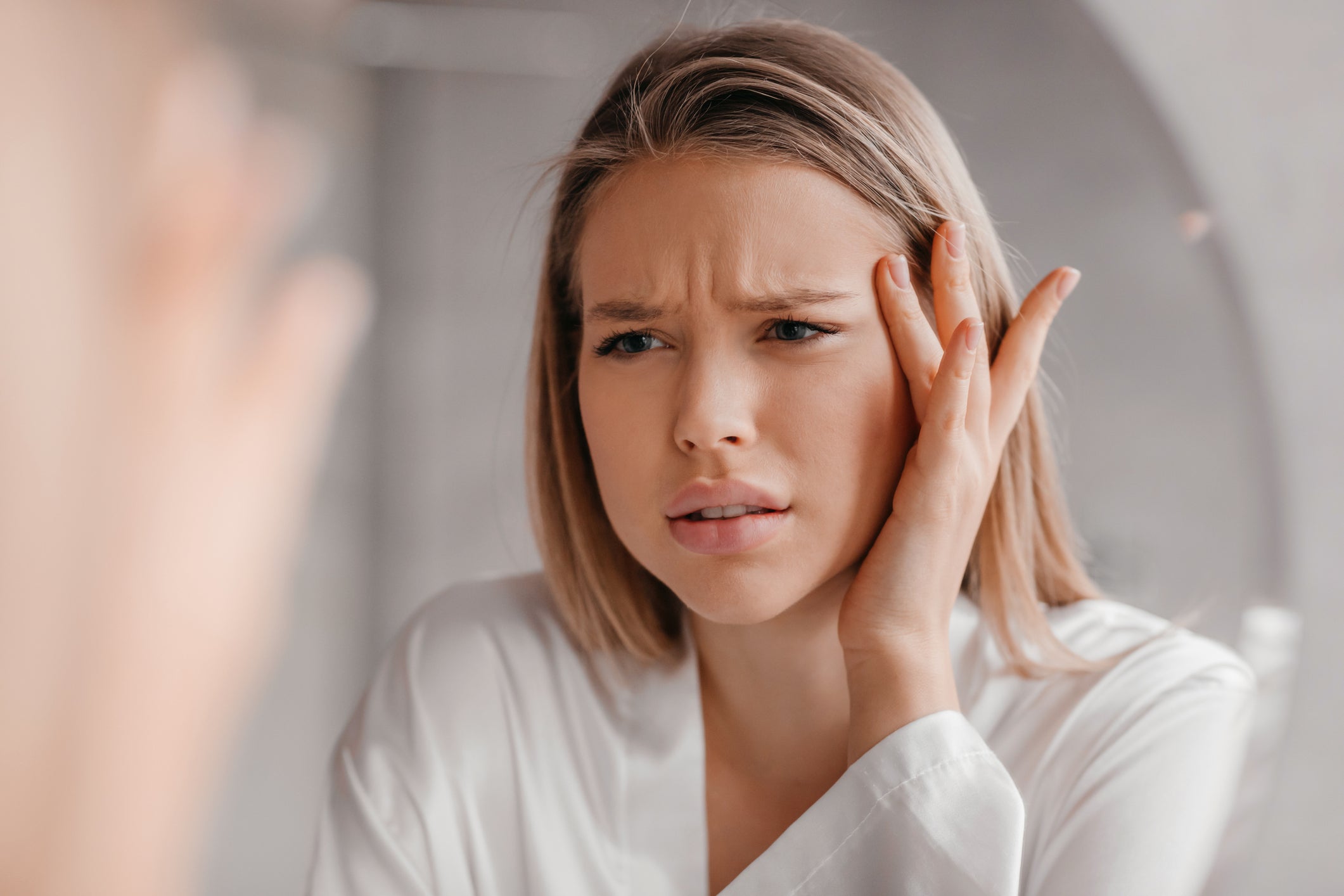 Frustrated blonde woman looking in mirror looking at her skin