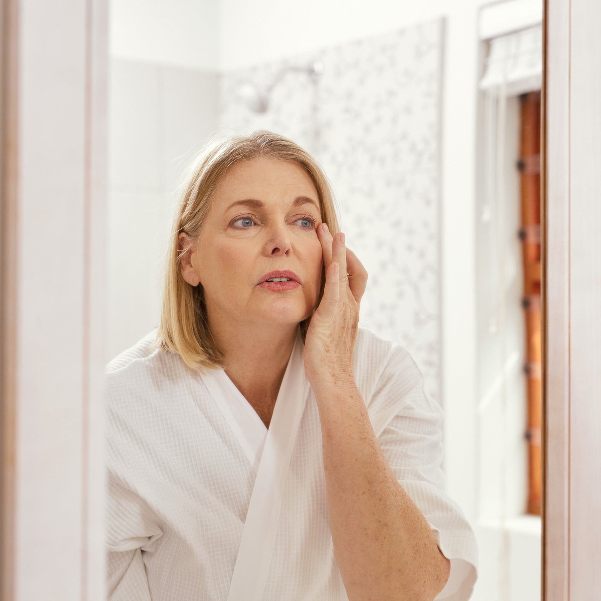 Woman looking into mirror at her dehydrated skin.
