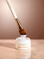 water balm with skincare brush on tan background marble top