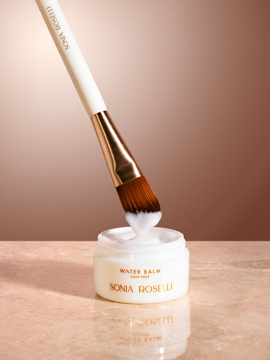 water balm with skincare brush on tan background marble top