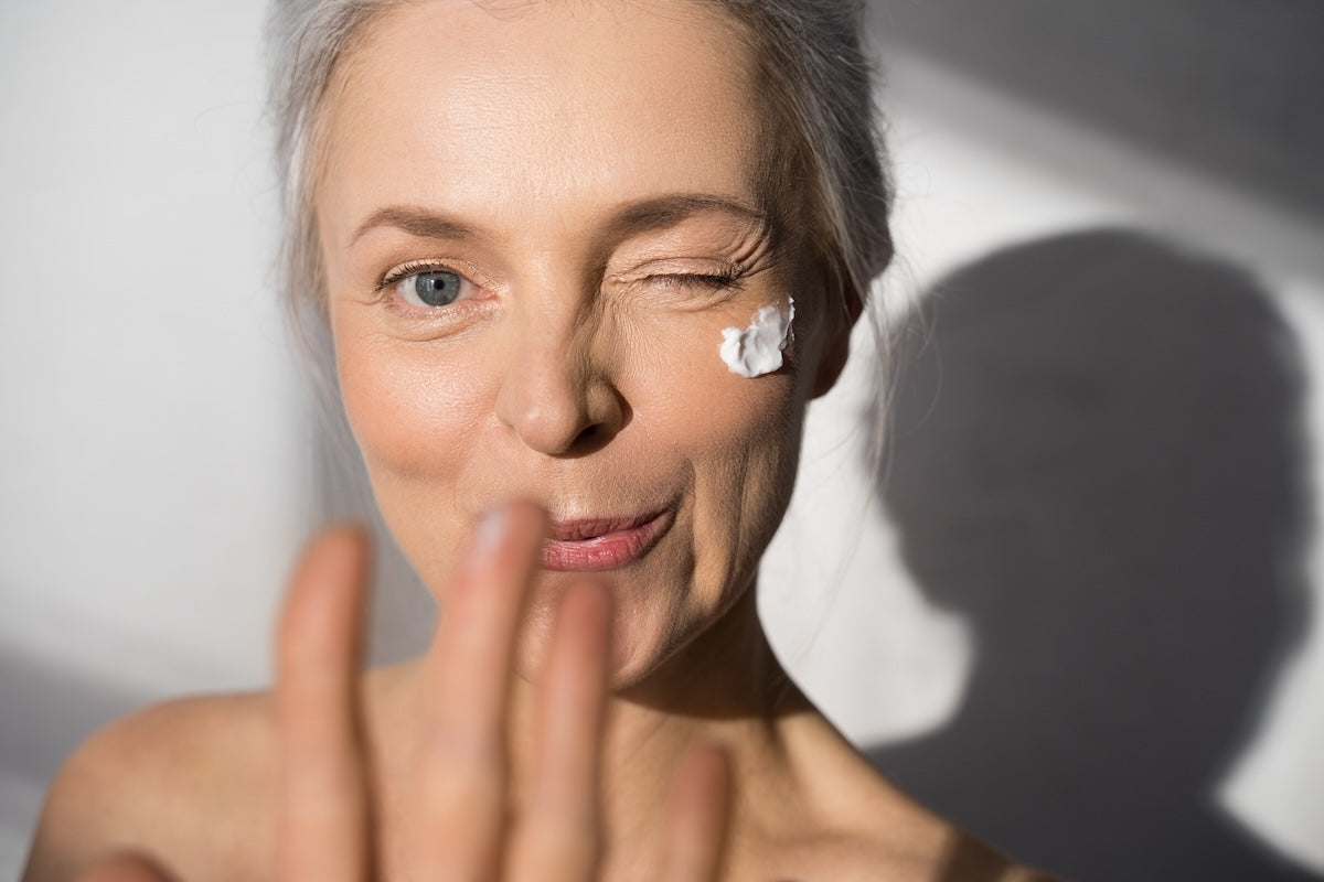 mature woman winking with skincare cream on her face.