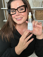 Sonia Roselli smiling and holding a Sonia Roselli Water Elixir Skin Prep bottle, showcasing radiant and hydrated skin.