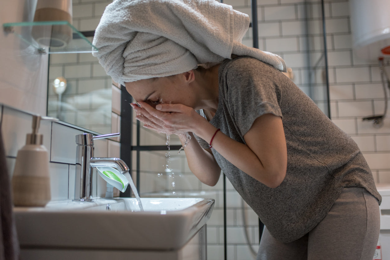 Woman with hair in towel washing face over sink