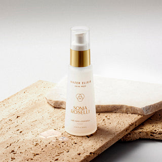 A white spray bottle labeled 'Sonia Roselli' placed on a textured stone surface. Ceramide essence that deeply hydrates and preps skin for better product absorption - fragrance-free for sensitive skin
